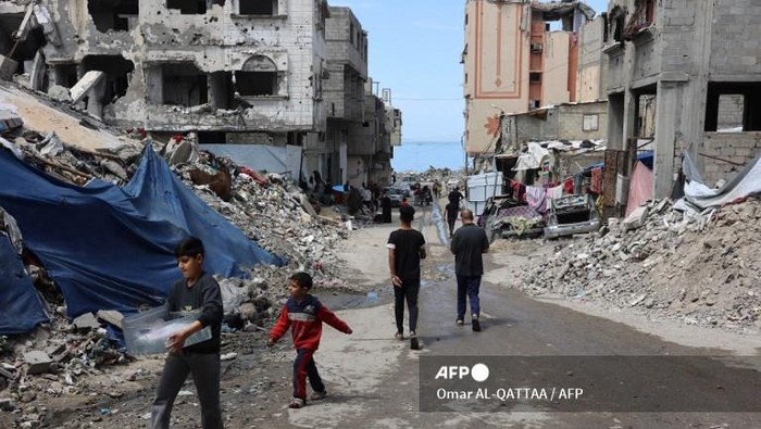 Palestinians walk past debris of buildings destroyed during the Israel-Hamas war, in Gaza City on March 28, 2025. Palestinian sources close to Hamas told AFP that talks were underway between the militant group and mediators from Egypt and Qatar on March 27, to revive a ceasefire and hostage release deal for Gaza. (Photo by Omar AL-QATTAA / AFP)