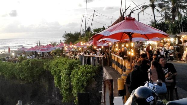 Pengunjung menikmati pesona batu karang hitam dan sunset di kafe dekat Pantai Cemagi, Kecamatan Mengwi, Badung, saat libur Idul Fitri, Senin (31/3/2025). (Agus Eka/detiBali)