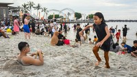 Pengunjung membenamkan tubuhnya dalam pasir di Pantai Lagoon Ancol, Jakarta, Selasa (1/4/2025). ANTARA FOTO/Sulthony Hasanuddin