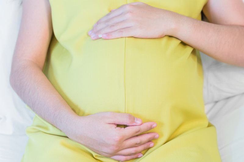 Pregnant woman touching her belly sitting on the bed in bedroom