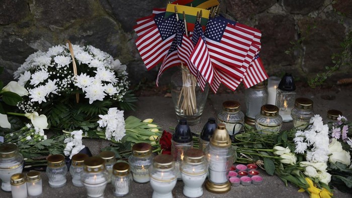 People with U.S. national flag come to pay their last respect to the three soldiers found dead on Monday at a training range in Pabrade, near the U.S. Embassy in Vilnius, Lithuania, Tuesday, April 1, 2025. (AP Photo/Mindaugas Kulbis)