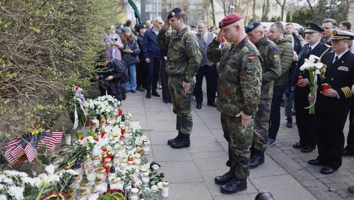 People with U.S. national flag come to pay their last respect to the three soldiers found dead on Monday at a training range in Pabrade, near the U.S. Embassy in Vilnius, Lithuania, Tuesday, April 1, 2025. (AP Photo/Mindaugas Kulbis)
