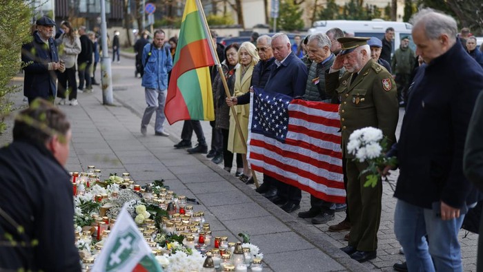 People with U.S. national flag come to pay their last respect to the three soldiers found dead on Monday at a training range in Pabrade, near the U.S. Embassy in Vilnius, Lithuania, Tuesday, April 1, 2025. (AP Photo/Mindaugas Kulbis)