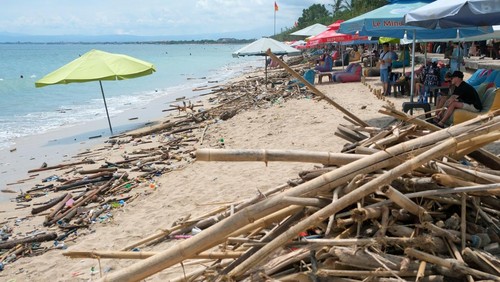 Wisatawan bersantai di dekat sampah kayu dan plastik  yang terbawa gelombang tinggi saat cuaca ekstrem di pesisir Pantai Kuta, Badung, Bali, Kamis (3/4/2025). Badan Meteorologi, Klimatologi, dan Geofisika mengeluarkan peringatan dini untuk masyarakat mengenai waspada potensi tingginya gelombang laut melebihi dua meter di perairan selatan Bali yang diperkirakan terjadi hingga Jumat (4/4/2025). ANTARA FOTO/Nyoman Hendra Wibowo/rwa.