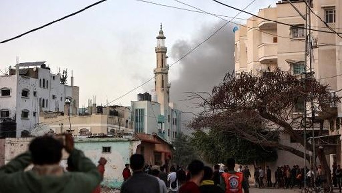 People and Palestinian rescuers watch as smoke rises after an Israeli strike hit a school in the al-Tuffah neighbourhood in Gaza City on April 3, 2025. Gazas civil defence agency said at least 21 people were killed on April 3 in an Israeli air strike on a school serving as a shelter for people displaced by the war. (Photo by Omar AL-QATTAA / AFP)