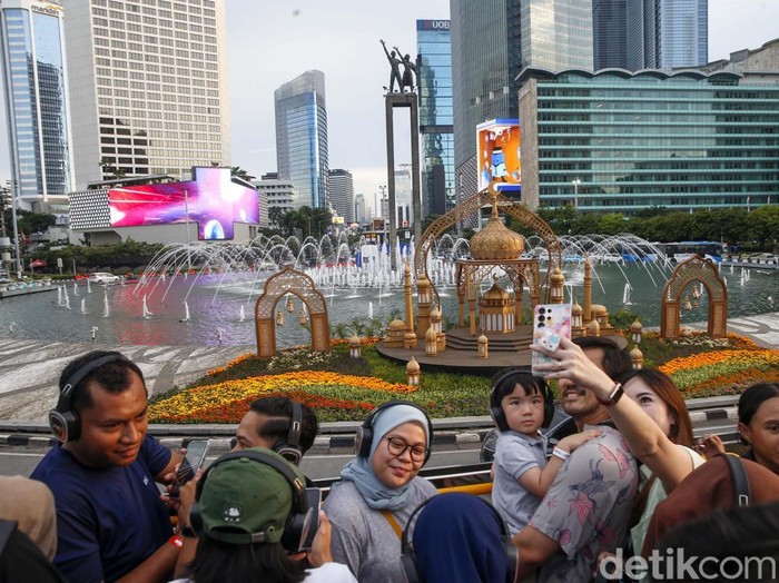 Pengunjung berswafoto dengan latar suasana kota dari atas bus wisata Open Top Tour of Jakarta di Jalan Jenderal Sudirman, Jakarta, Jumat (4/4/2025). Wisata bus dengan rute yang melewati landmark Kota Jakarta menjadi salah satu destinasi warga untuk mengisi waktu libur Lebaran 2025.