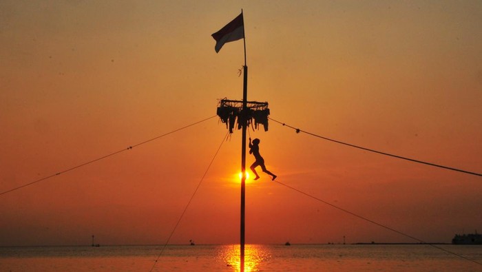 Peserta mengibarkan bendera merah putih saat mengikuti lomba panjat pinang di kawasan Pantai Demaan, Kelurahan Demaan, Jepara, Jawa Tengah, Senin (7/4/2025). Lomba panjat pinang yang digelar nelayan setempat sepekan setelah Hari Raya Idul Fitri itu untuk memeriahkan tradisi Syawalan atau Lebaran Ketupat sekaligus untuk menjalin kebersamaan serta untuk menarik wisatawan. ANTARA FOTO/Yusuf Nugroho/YU