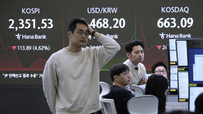 Currency traders work near a screen showing the Korea Composite Stock Price Index (KOSPI), top left, and the foreign exchange rate between U.S. dollar and South Korean won, top center, at the foreign exchange dealing room of the KEB Hana Bank headquarters in Seoul, South Korea, Monday, April 7, 2025. (AP Photo/Ahn Young-joon)