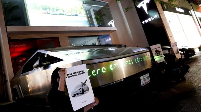 Gelombang Protes Melanda Dealer-dealer Tesla di Berbagai Negara People hold posters reading