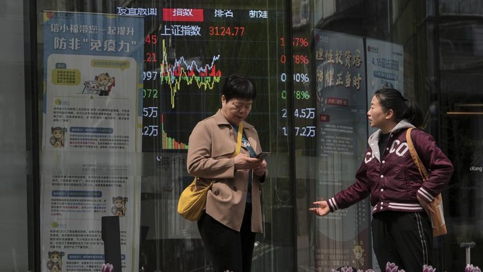 Women talk near an electronic board displaying Shanghai shares trading index at a brokerage house, in Beijing, Tuesday, April 8, 2025. (AP Photo/Andy Wong)