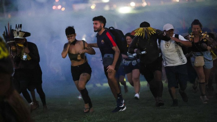 A firefighter assists an Indigenous woman who is affected by tear gas fired by riot police while taking part in the Terra Livre (Free Land) protest camp to demand the demarcation of land and to defend cultural rights, in Brasilia, Brazil April 10, 2025. REUTERS/Adriano Machado