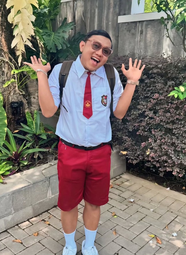 Denny Caknan tampil dengan seragam SD lengkap dengan dasi dan ikat pinggang hitam. Ia juga mengenakan kaos kaki sebetis dan sepasang sepatu putih. Sambil membawa tas ransel dan dengan rambut klimis, Denny memamerkan pose imutnya ke arah kamera.  Foto: Instagram/@denny_caknan