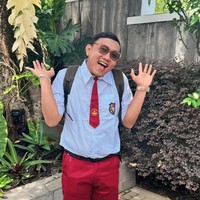 Denny Caknan tampil dengan seragam SD lengkap dengan dasi dan ikat pinggang hitam. Ia juga mengenakan kaos kaki sebetis dan sepasang sepatu putih. Sambil membawa tas ransel dan dengan rambut klimis, Denny memamerkan pose imutnya ke arah kamera.  Foto: Instagram/@denny_caknan