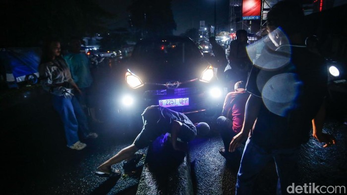 Jalan yang licin setelah hujan dan lampu jalan yang mati membuat sebuah mobil tersangkut separator di Bekasi, Jumat (11/4/2025). Warga pun gotong-royong melakukan evakuasi.