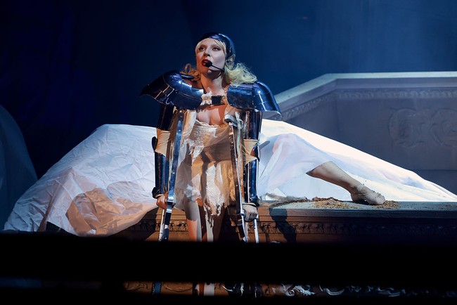 Membuka penampilannya, Lady Gaga muncul di atas panggung sebagai sang ‘Mistress’, mengenakan wig bob hitam dan gaun merah raksasa bertingkat. Gaun tersebut bukan hanya dramatis dalam ukuran, tapi juga menyembunyikan para penari di balik roknya yang mengembang, lengkap dengan detail menyerupai tanduk di kerah dan pergelangan tangan. Foto: Kevin Mazur/Getty Images for Coa/Kevin Mazur