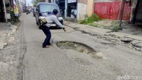 Seorang warga sedang mengingatkan pengendara yang melintasi jalan rusak di Desa Tambakrejo, Kecamatan Waru.