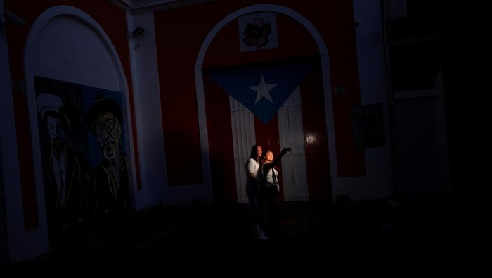A couple take a selfie in front of a Puerto Rican flag after the country was hit with a massive power outage where energy plants across the island unexpectedly shut down, in San Juan, Puerto Rico April 16, 2025.  REUTERS/Ricardo Arduengo     TPX IMAGES OF THE DAY