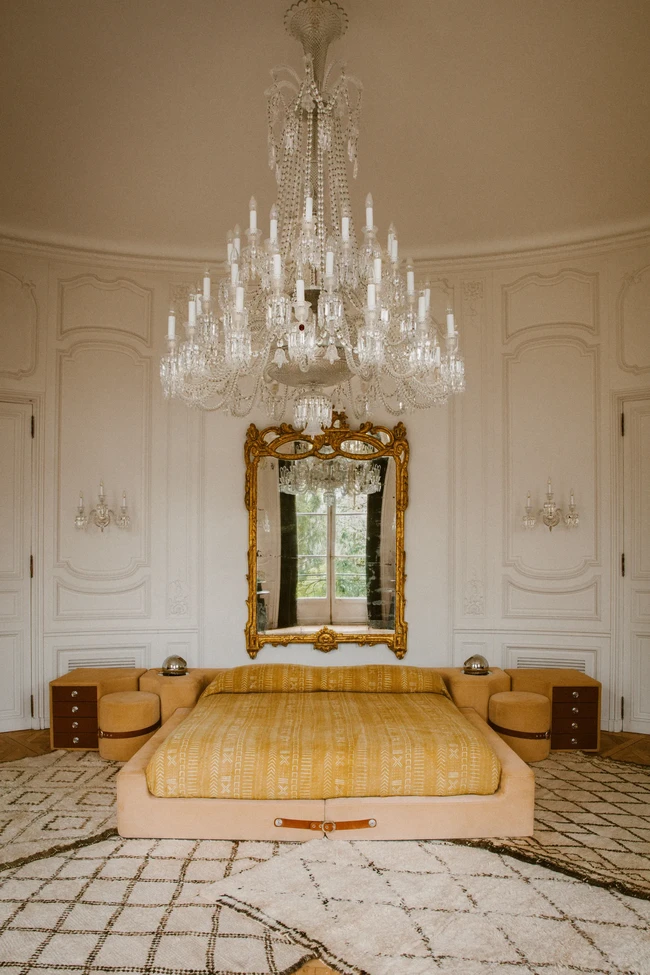 Lampu gantung dan cermin berbingkai emas menciptakan atmosfer dramatis di kamar utama. Untuk menyeimbangkannya, ayah aktris Zoe Kravitz ini memilih tempat tidur yang minimalis.  (Foto: Architectural Digest/Matthieu Salvaing)
