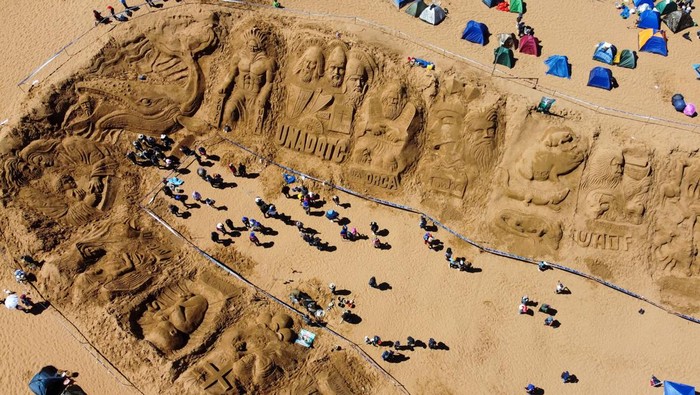 Aksi Seniman Memahat Adegan Alkitab di Bukit Pasir Bolivia An Aymara woman looks on as visual artists work on a sand sculpture depicting biblical scenes during Holy Week celebrations at the Arenales of Cochiraya, on the outskirts of Oruro, Bolivia April 18, 2025. REUTERS/Claudia Morales TPX IMAGES OF THE DAY