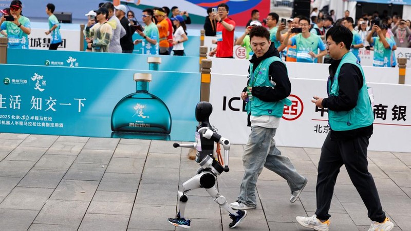Engineers run with the humanoid robot as it participates along with human runners in the E-Town Half Marathon & Humanoid Robot Half Marathon in Beijing, China April, 19 2025. REUTERS/Tingshu Wang