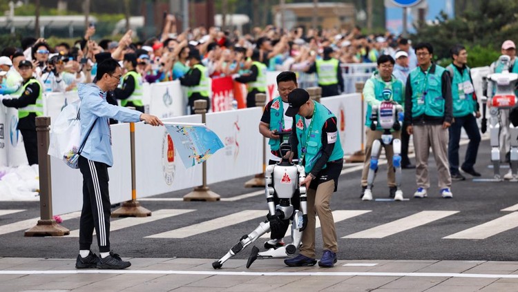 Engineers run with the humanoid robot as it participates along with human runners in the E-Town Half Marathon & Humanoid Robot Half Marathon in Beijing, China April, 19 2025. REUTERS/Tingshu Wang