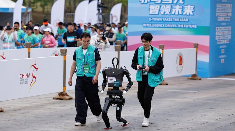 Engineers run with the humanoid robot as it participates along with human runners in the E-Town Half Marathon & Humanoid Robot Half Marathon in Beijing, China April, 19 2025. REUTERS/Tingshu Wang