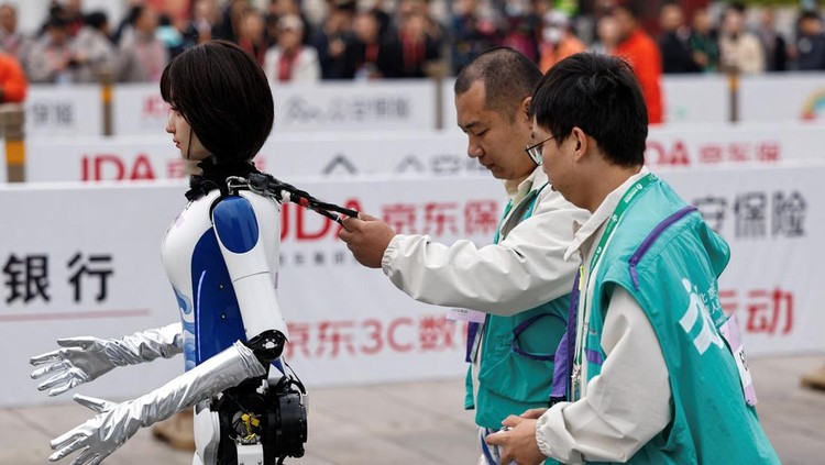 Engineers run with the humanoid robot as it participates along with human runners in the E-Town Half Marathon & Humanoid Robot Half Marathon in Beijing, China April, 19 2025. REUTERS/Tingshu Wang