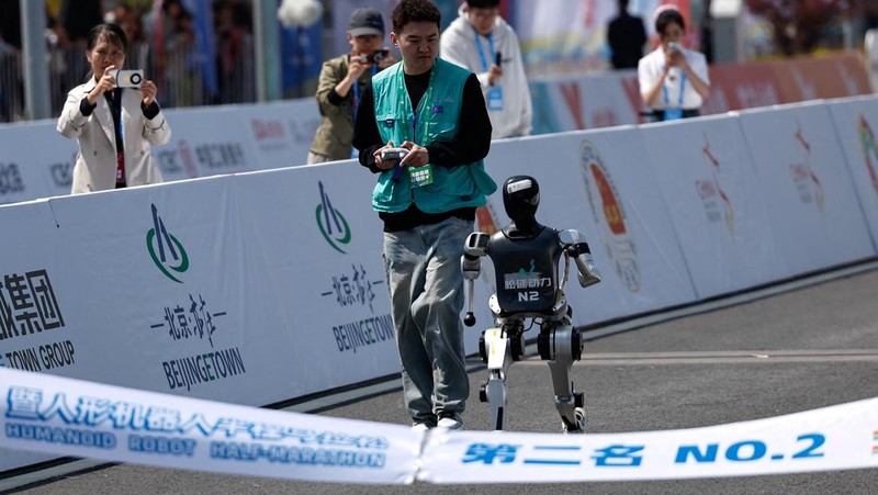Engineers run with the humanoid robot as it participates along with human runners in the E-Town Half Marathon & Humanoid Robot Half Marathon in Beijing, China April, 19 2025. REUTERS/Tingshu Wang
