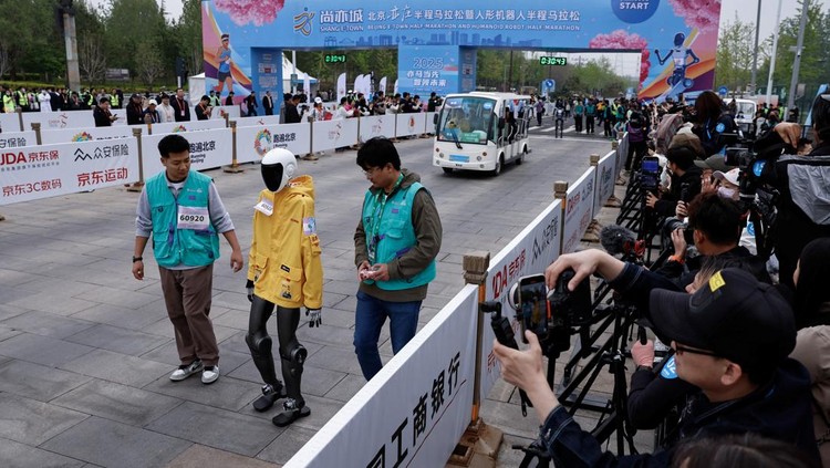 Engineers run with the humanoid robot as it participates along with human runners in the E-Town Half Marathon & Humanoid Robot Half Marathon in Beijing, China April, 19 2025. REUTERS/Tingshu Wang