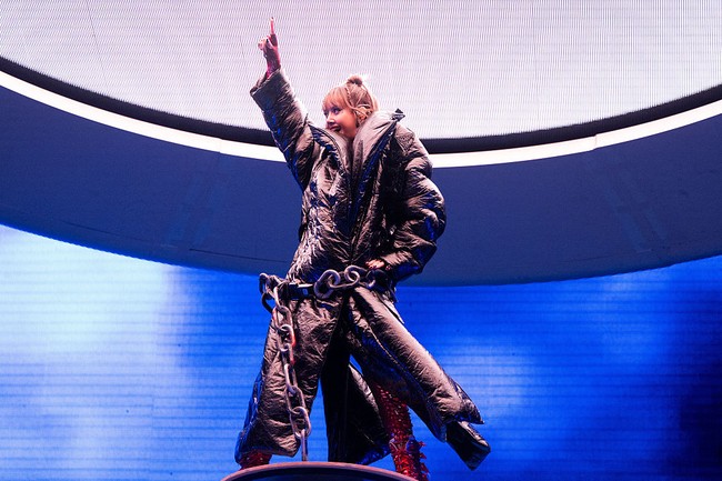 Dalam salah satu bagian paling teatrikal dari set panggungnya, pelantun lagu ‘Born Again’ ini memakai jaket puffer raksasa mengilap di atas bodysuit merah tersebut. Dia tampak berdiri gagah di atas platform tinggi, dengan rantai besar melingkar di pinggangnya, menambah kesan panggung yang megah dan intens. Foto: Getty Images