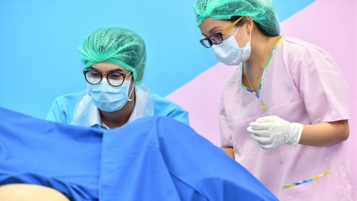 Asian male obstetrician and nurse are delivered to the patient lying on a bed in the delivery room of the hospital