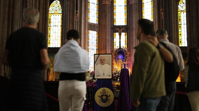Umat Katolik di Dunia Meratapi Kepergian Paus Fransiskus People stand next to a photograph of Pope Francis placed at Saint Anthony Catholic church in Istanbul, Turkey, Monday, April 21, 2025. (AP Photo/Khalil Hamra)