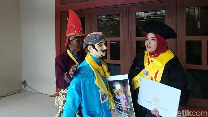 Budi Prasojo (68) memberikan kejutan kepada anak menantunya, Sarly Puspita Ariesta, yang ikut wisuda pascasarjana hari ini di GSP UGM, Rabu (23/4/2025).