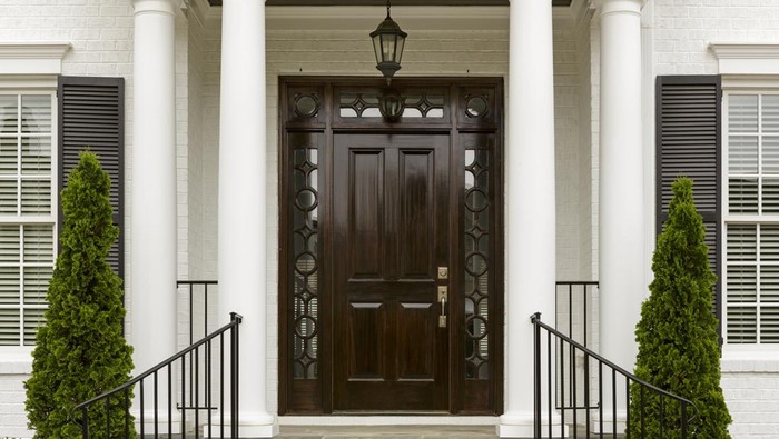 A grand entrance way leading up to an ornate dark wood door with green trees.
