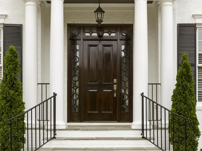 A grand entrance way leading up to an ornate dark wood door with green trees.