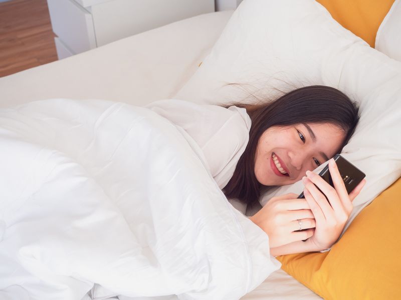 asian girl wake up on bed and playing with the mobile phone