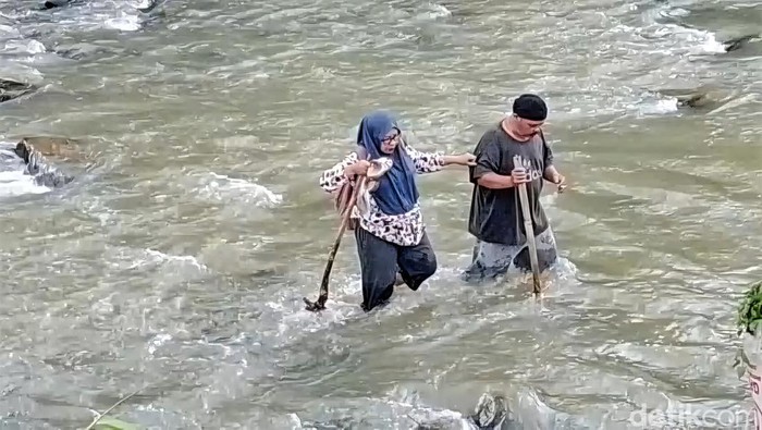 Warga melintasi derasnya air Sungai Cikaso Sukabumi.