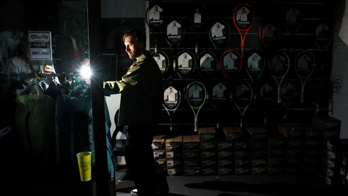 Listrik di Wilayah Spanyol Tiba-tiba Padam Tennis - Madrid Open - Park Manzanares, Madrid, Spain - April 28, 2025 A man uses his cell phone's flashlight in a dark sports shop after the matches get suspended due to a power outage REUTERS/Violeta Santos Moura