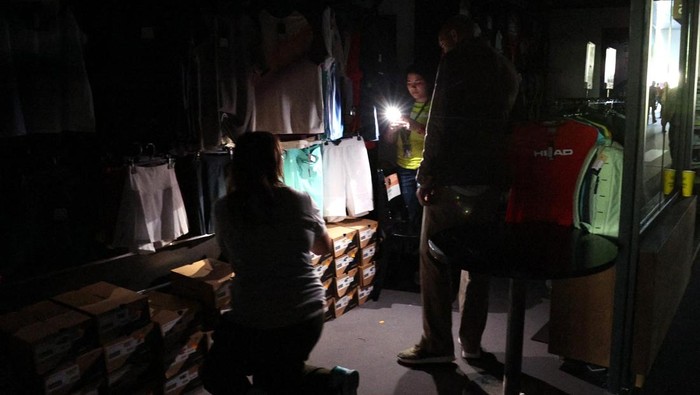 Listrik di Wilayah Spanyol Tiba-tiba Padam Tennis - Madrid Open - Park Manzanares, Madrid, Spain - April 28, 2025 A man uses his cell phone's flashlight in a dark sports shop after the matches get suspended due to a power outage REUTERS/Violeta Santos Moura
