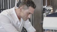 Mengenakan kemeja putih, artis yang lahir di Tasikmalaya ini juga sedang serius membuat kopi. Indra Bruggman terlihat sedang memegang portafilter di mesin espresso. Foto: Instagram @indrabruggman