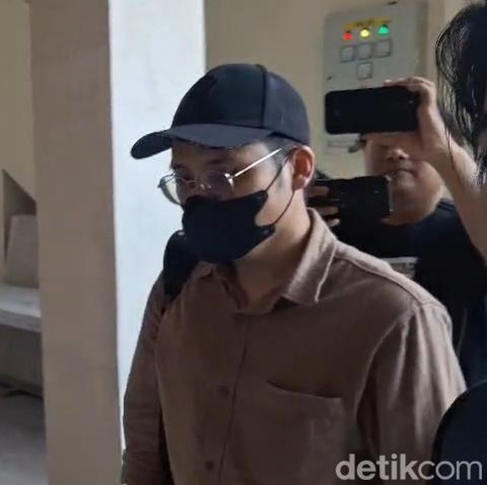 Dokter YA (bertopi dan bermasker) saat memenuhi panggilan pemeriksaan di Polresta Malang Kota.