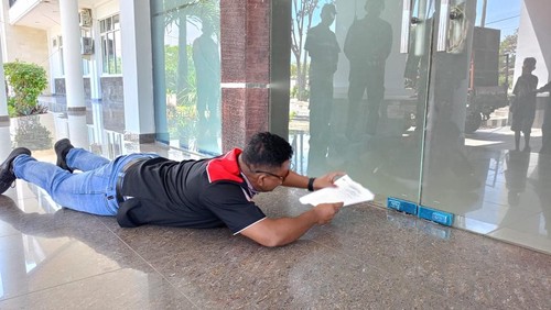 Ketua FSBDSI Manggarai Barat Rafael Taher merayap saat menyelipkan pernyataan sikap butuh lewat kolong di bawah pintu kantor DPRD Manggarai Barat, Kamis (1/5/2025). (Foto: Dok. FSBDSI Manggarai Barat)