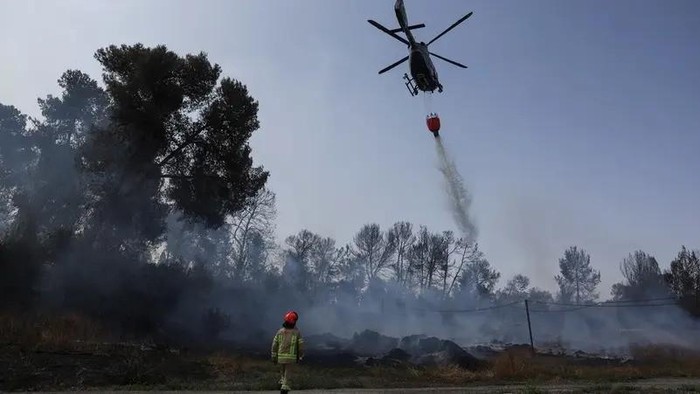 A firefighter walks as a helicopter drops water, a day after wildfires broke out due to extreme heat and winds, in Latrun, central Israel, May 1, 2025. (Reuters)