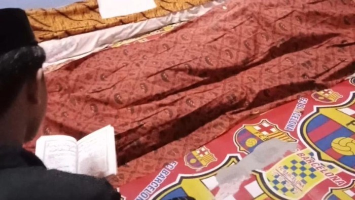 Seorang anak membacakan yasin di depan jenazah ibu dan ayahnya