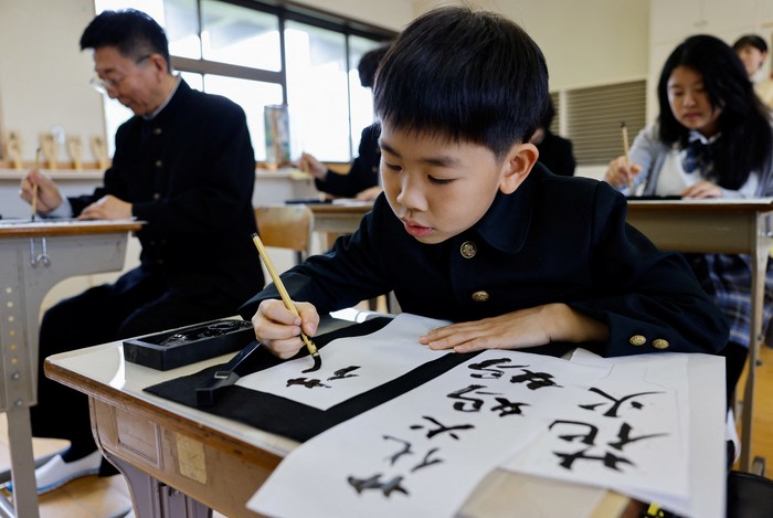 Tourists from abroad wearing school uniforms listen to a woman playing a teacher at a class room while taking part in a Japanese high school experience in Kimitsu, Chiba prefecture, Japan April 23, 2025.  REUTERS/Manami Yamada