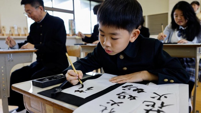 Tourists from abroad wearing school uniforms listen to a woman playing a teacher at a class room while taking part in a Japanese high school experience in Kimitsu, Chiba prefecture, Japan April 23, 2025.  REUTERS/Manami Yamada
