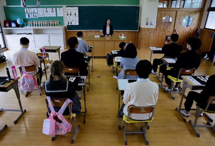 Tourists from abroad wearing school uniforms listen to a woman playing a teacher at a class room while taking part in a Japanese high school experience in Kimitsu, Chiba prefecture, Japan April 23, 2025.  REUTERS/Manami Yamada
