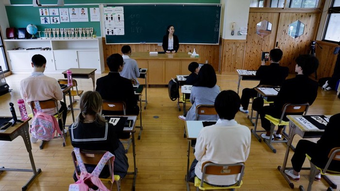 Sensasi Menjadi Siswa Sekolah di Jepang Tourists from abroad wearing school uniforms listen to a woman playing a teacher at a class room while taking part in a Japanese high school experience in Kimitsu, Chiba prefecture, Japan April 23, 2025. REUTERS/Manami Yamada