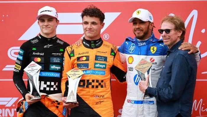 MIAMI, FLORIDA - MAY 03: Sprint winner Lando Norris of Great Britain and McLaren Second placed Oscar Piastri of Australia and McLaren and Third placed Lewis Hamilton of Great Britain and Scuderia Ferrari are presented with thier trophies by Jerry Bruckheimer during the Sprint ahead of the F1 Grand Prix of Miami at Miami International Autodrome on May 03, 2025 in Miami, Florida.   Hector Vivas/Getty Images/AFP (Photo by Hector Vivas / GETTY IMAGES NORTH AMERICA / Getty Images via AFP)
