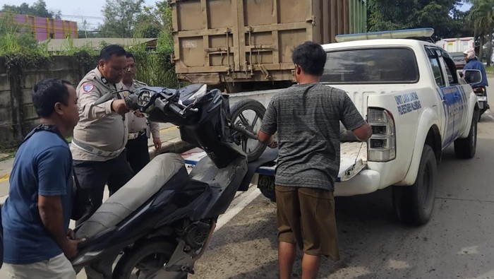 Petugas kepolisian dibantu warga mengevakuasi motor pasutri yang tabrak turk parkir di pinggir jalan